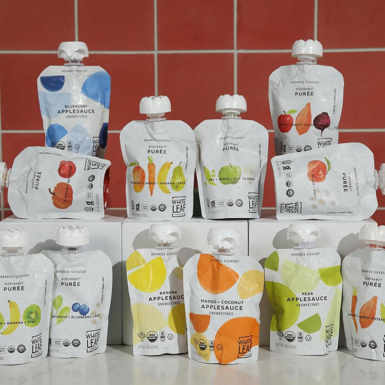Assorted pouches of White Leaf puree and applesauce on a tiled wall background