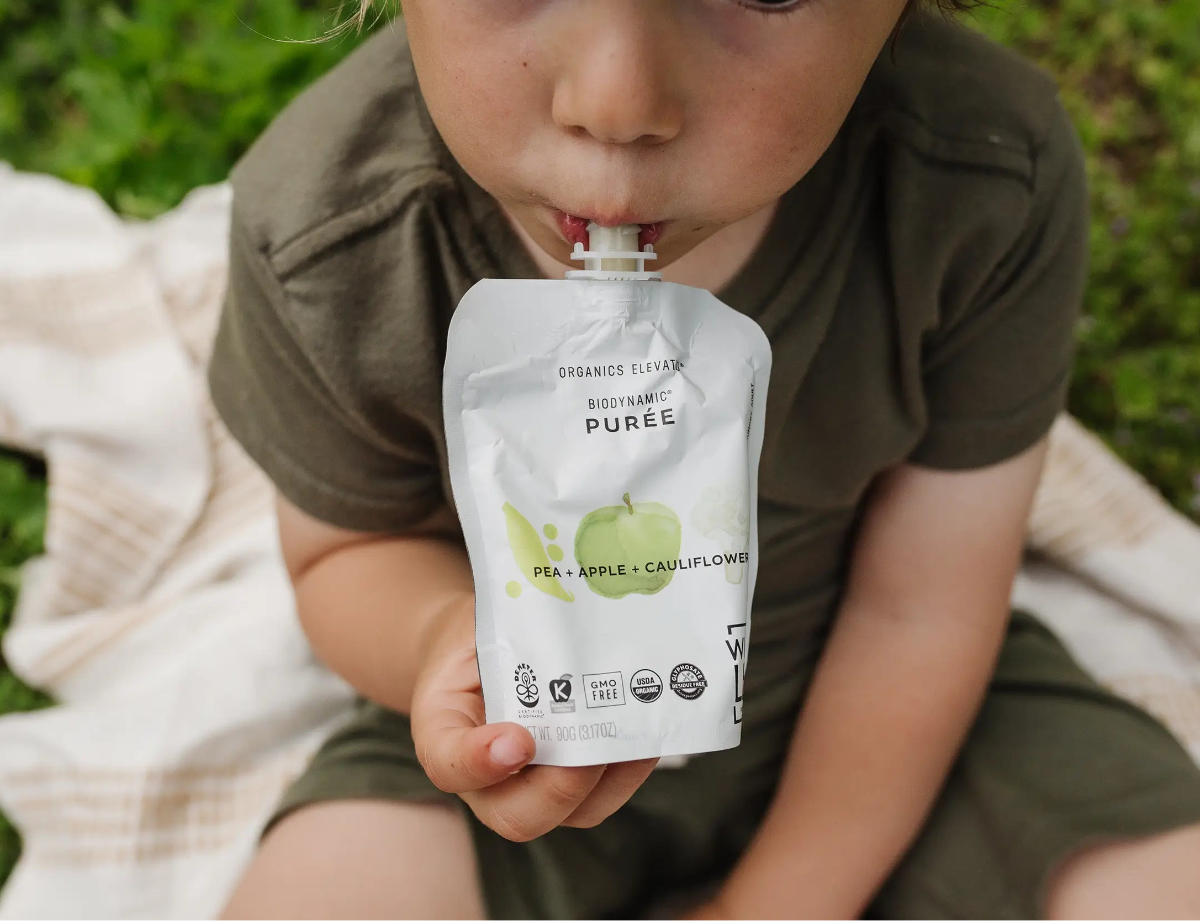 Child holding a pouch of organic baby food outdoors