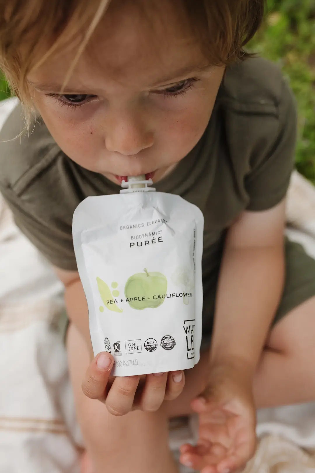 Child holding a pouch of organic baby food puree Pea + Apple + Cauliflower flavor by White Leaf Provisions