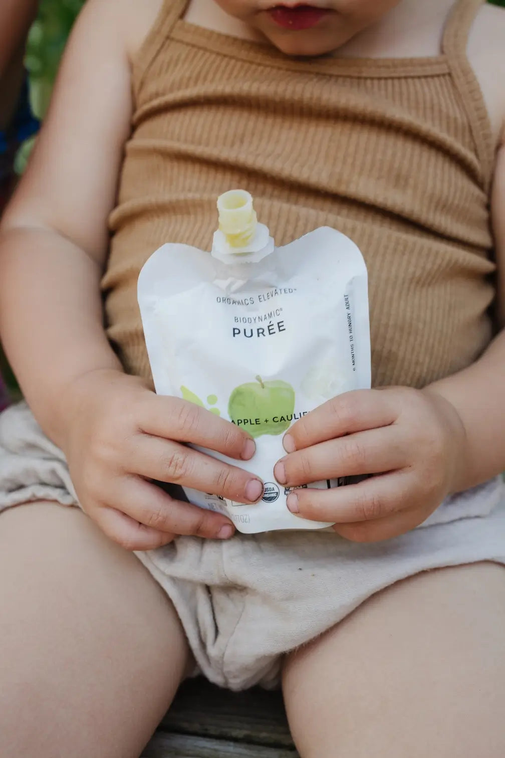 Child holding a toddler snack pouch of apple and cauliflower puree by White Leaf Provisions